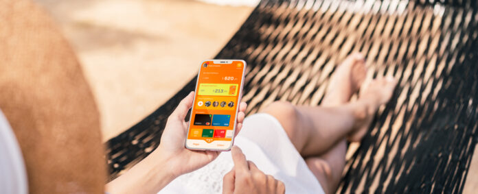 Young woman traveler lying on a hammock and using smartphone at the beach while traveling for summer vacation