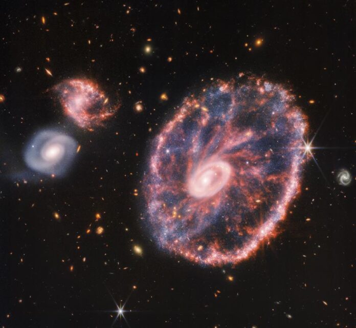 La potente mirada infrarroja del telescopio James Webb ha logrado una instantánea detallada de Rueda de Carro, pero también de dos galaxias compañeras más pequeñas con un telón de fondo de muchas otras galaxias. EFE