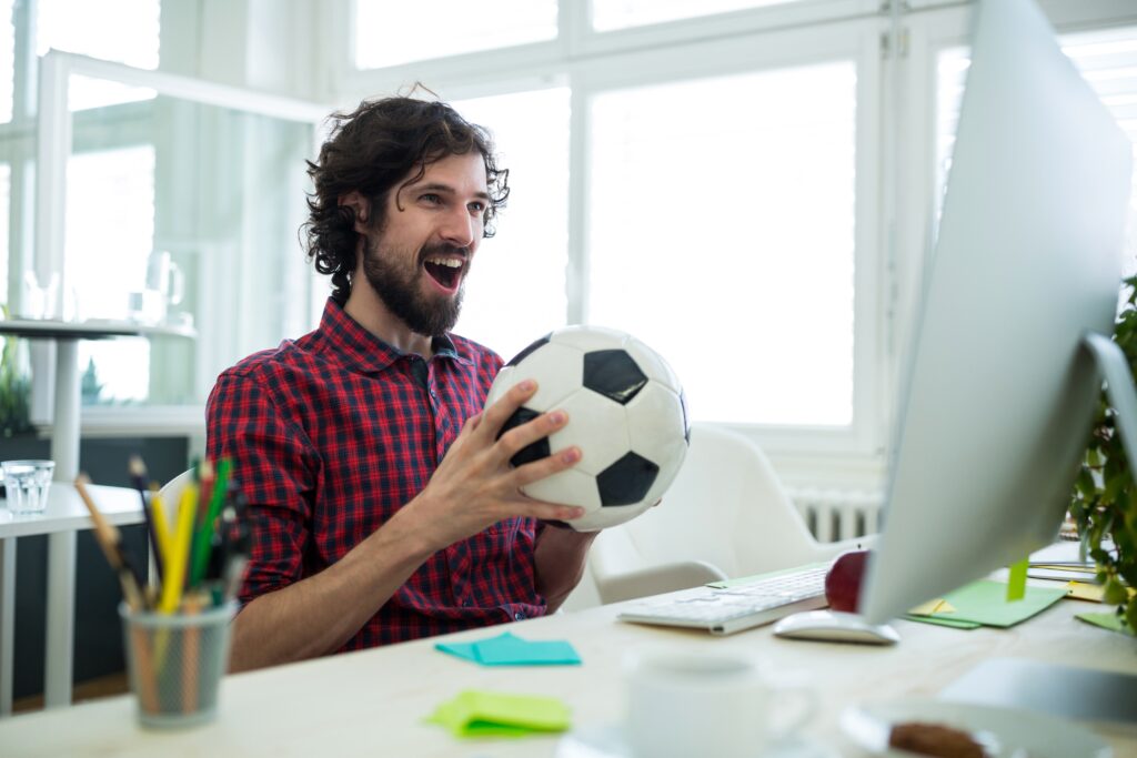 Male graphic designer cheering while watching football match in office thumbnail