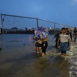 Personas caminan por una vía inundada debido a fuertes lluvias este martes. En el país registran 2.000 afectados.