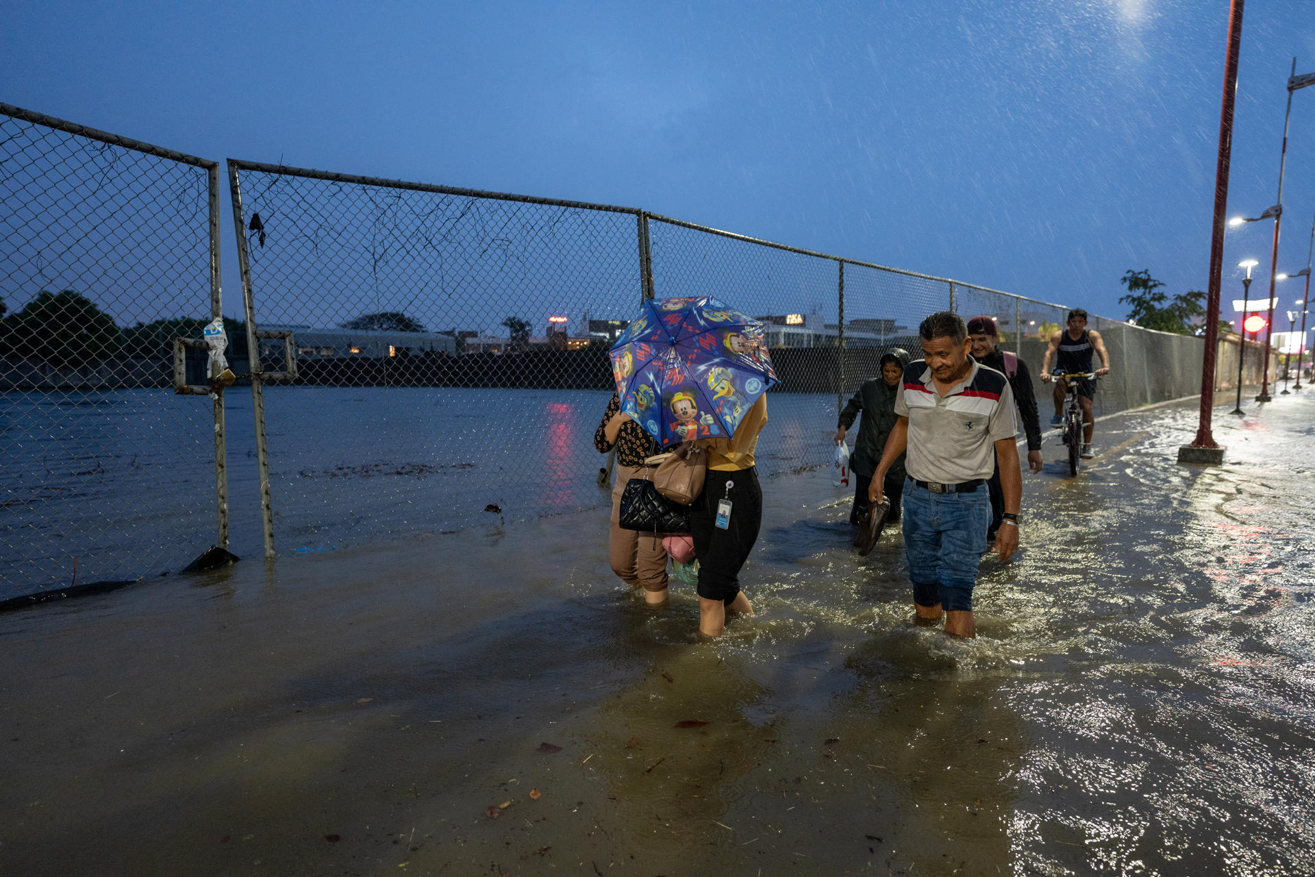 Personas caminan por una vía inundada debido a fuertes lluvias este martes. En el país registran 2.000 afectados.