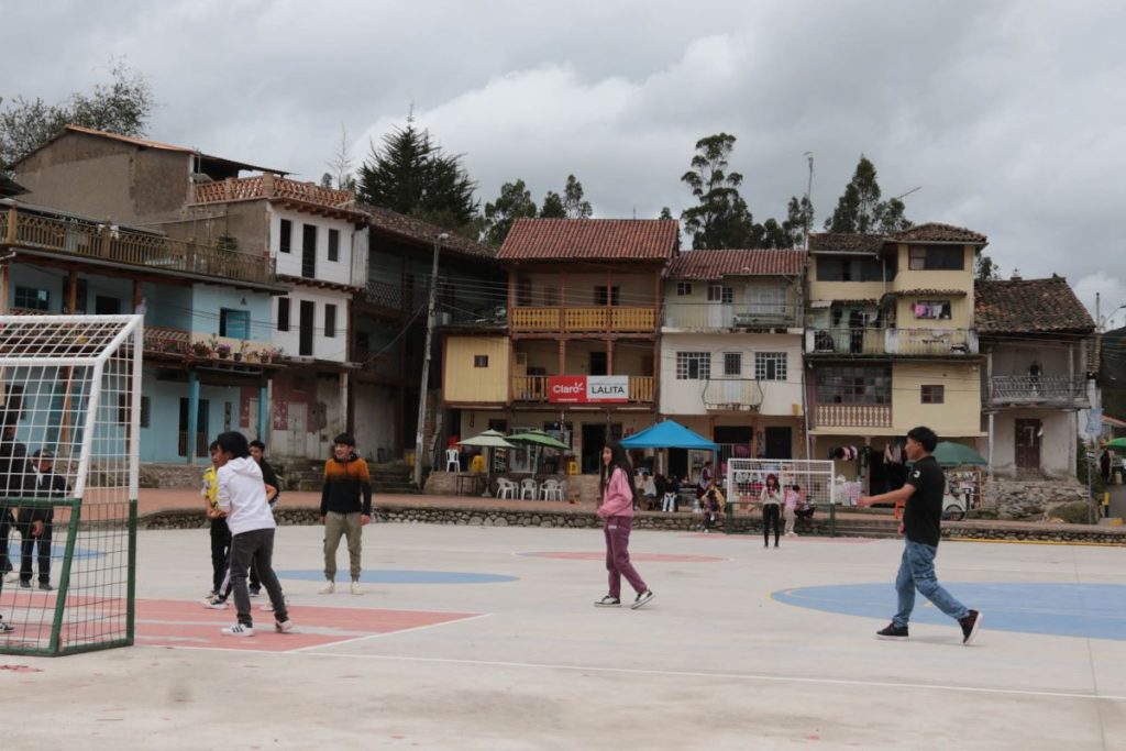 Niños juegan en la cancha del centro parroquial de Quingeo, rodeados por casas de adobe y bahareque que conservan la arquitectura vernácula del lugar.